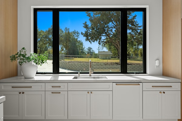 Modern kitchen sink with cabinets and a large window overlooking greenery